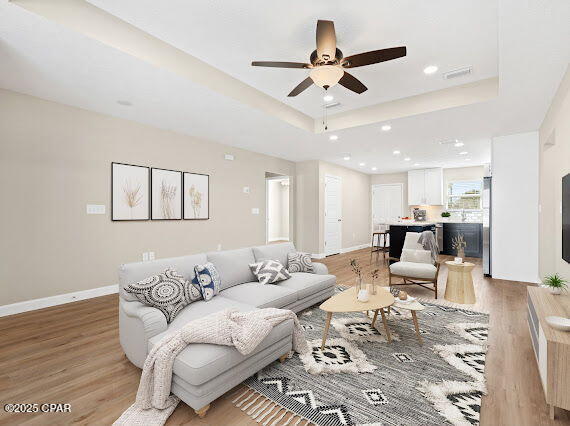 living room with a tray ceiling, light hardwood / wood-style floors, and ceiling fan