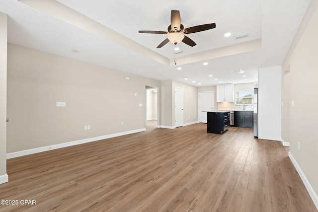 unfurnished living room featuring hardwood / wood-style flooring, ceiling fan, and a raised ceiling