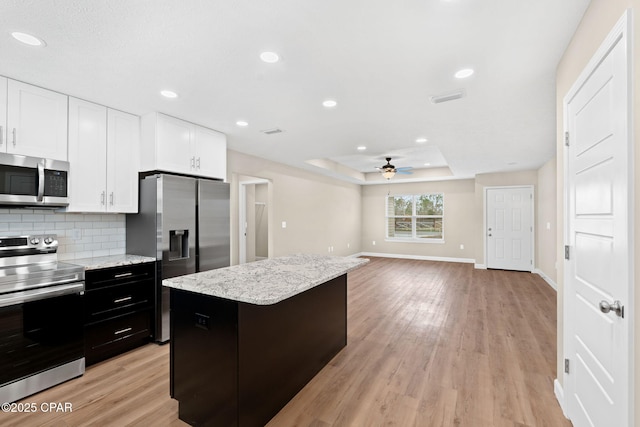 kitchen featuring white cabinetry, appliances with stainless steel finishes, a raised ceiling, a kitchen island, and light hardwood / wood-style floors