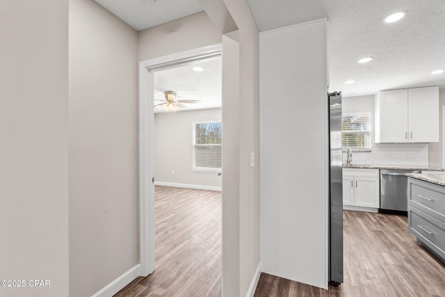 kitchen with a textured ceiling, wood finished floors, white cabinetry, appliances with stainless steel finishes, and decorative backsplash