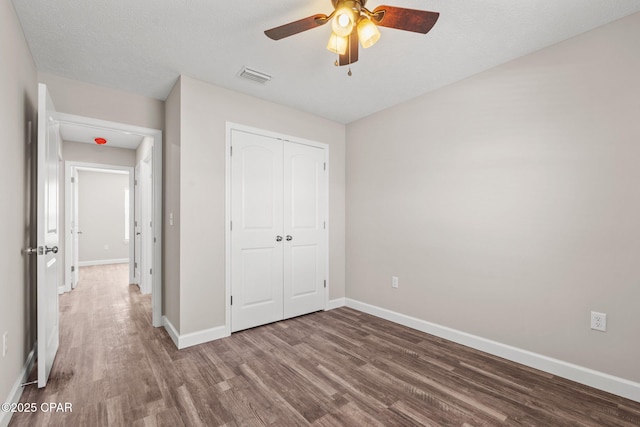 unfurnished bedroom featuring ceiling fan, visible vents, baseboards, a closet, and dark wood finished floors