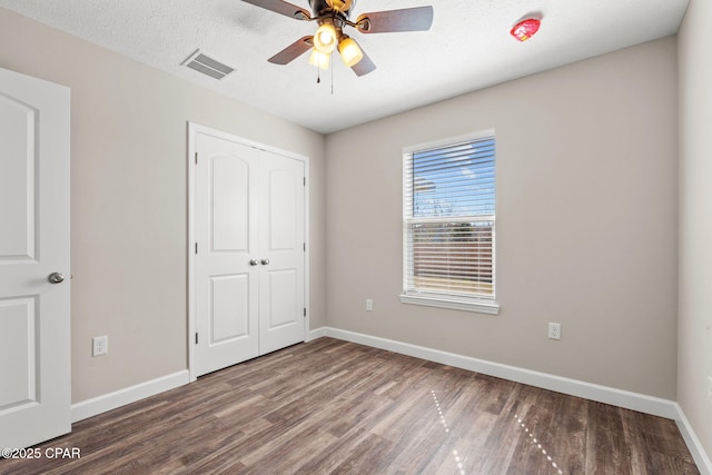 unfurnished bedroom featuring dark wood-type flooring, a closet, visible vents, and baseboards