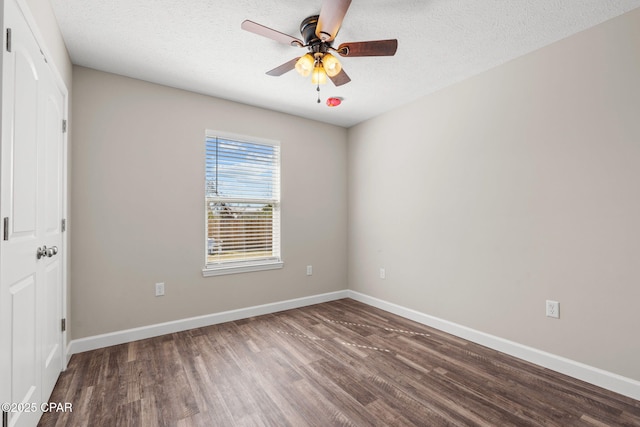 spare room featuring a textured ceiling, ceiling fan, dark wood finished floors, and baseboards