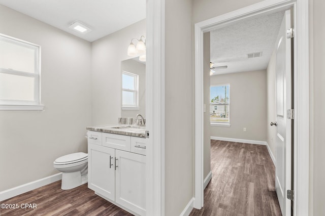 half bathroom featuring baseboards, visible vents, toilet, wood finished floors, and vanity