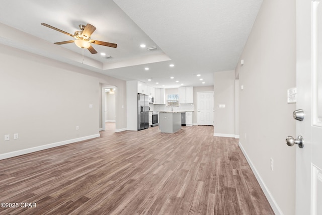 unfurnished living room featuring a tray ceiling, light wood finished floors, recessed lighting, and baseboards