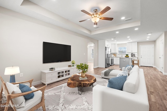 living area featuring a tray ceiling, recessed lighting, visible vents, light wood-type flooring, and baseboards