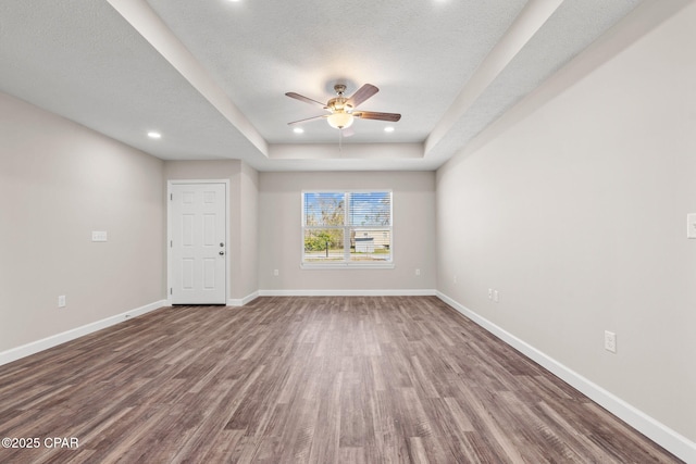 empty room featuring a tray ceiling, recessed lighting, baseboards, and wood finished floors