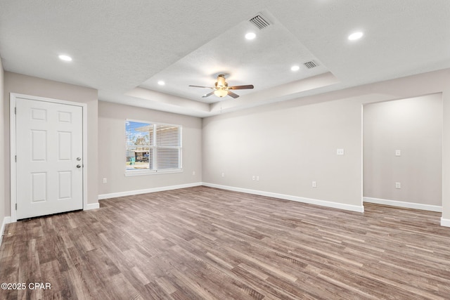 unfurnished living room with a raised ceiling, visible vents, a textured ceiling, light wood-type flooring, and baseboards