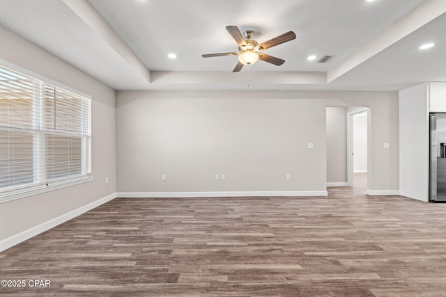 unfurnished room with visible vents, baseboards, a tray ceiling, light wood-style floors, and recessed lighting