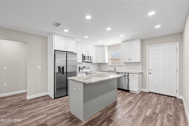 kitchen with appliances with stainless steel finishes, white cabinets, visible vents, and a kitchen island