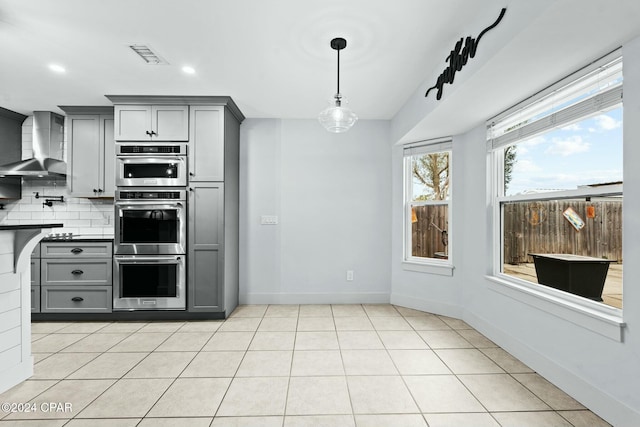 kitchen featuring gray cabinets, light tile patterned floors, tasteful backsplash, and wall chimney range hood