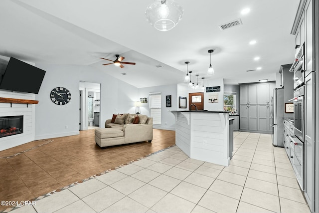 kitchen with light tile patterned floors, a kitchen bar, gray cabinetry, a large fireplace, and pendant lighting