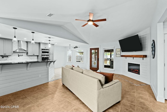 tiled living room featuring lofted ceiling, ceiling fan, and a large fireplace