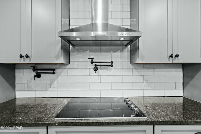 kitchen featuring tasteful backsplash, wall chimney range hood, black electric stovetop, and white cabinetry