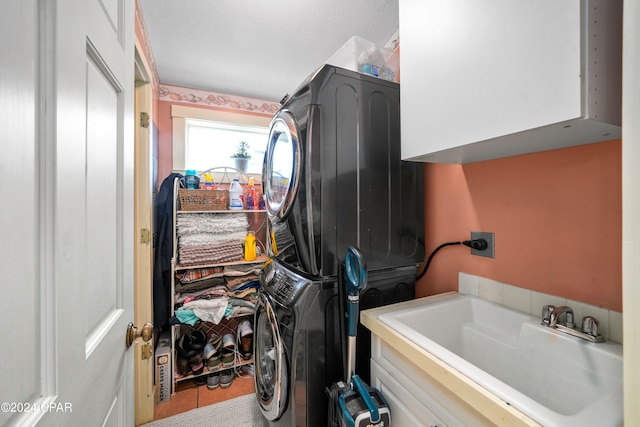 laundry area featuring tile patterned floors, cabinets, stacked washing maching and dryer, and sink