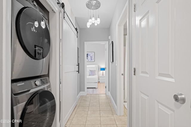 laundry area featuring a barn door, light tile patterned flooring, stacked washer / drying machine, and an inviting chandelier