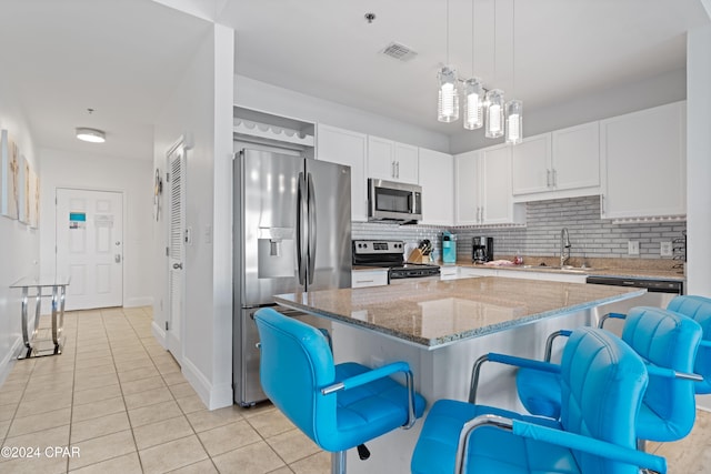 kitchen with appliances with stainless steel finishes, light stone counters, a kitchen island, white cabinetry, and a breakfast bar area