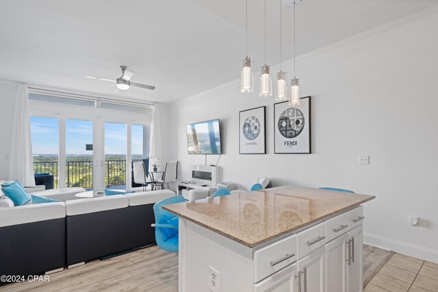 kitchen with ceiling fan, light wood-type flooring, decorative light fixtures, a kitchen island, and white cabinetry