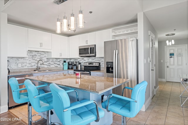 kitchen with stainless steel appliances, light stone counters, a chandelier, pendant lighting, and a kitchen island