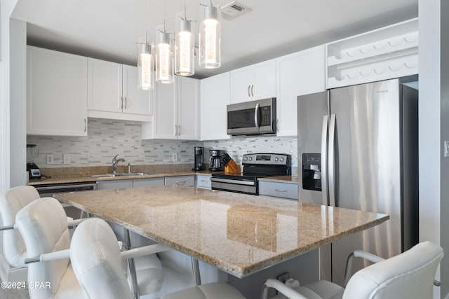 kitchen with a breakfast bar, stainless steel appliances, a kitchen island, sink, and white cabinetry