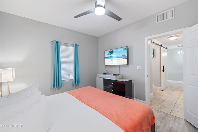 bedroom featuring a barn door, light hardwood / wood-style floors, and ceiling fan