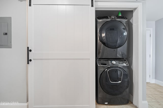 washroom with a barn door, light tile patterned flooring, electric panel, and stacked washer and clothes dryer