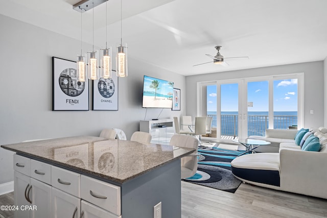 kitchen with ceiling fan, pendant lighting, stone counters, white cabinets, and light hardwood / wood-style floors