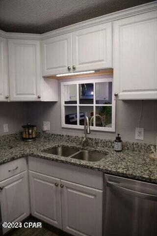 kitchen featuring a textured ceiling, sink, stone countertops, dishwasher, and white cabinetry