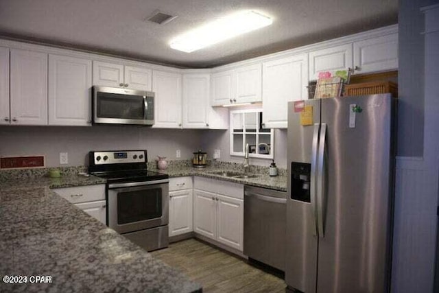 kitchen featuring white cabinets, sink, dark stone countertops, dark hardwood / wood-style flooring, and stainless steel appliances