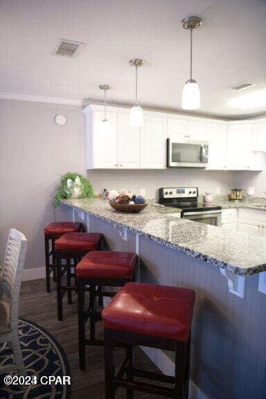 kitchen with appliances with stainless steel finishes, decorative light fixtures, a kitchen bar, and white cabinets