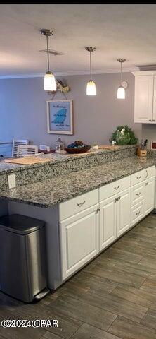 kitchen with ornamental molding, dark stone counters, decorative light fixtures, dark hardwood / wood-style floors, and white cabinetry