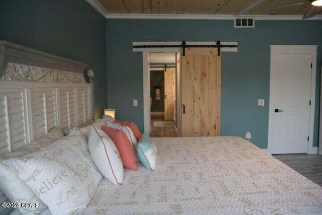 bedroom with crown molding, wooden ceiling, a barn door, and hardwood / wood-style flooring