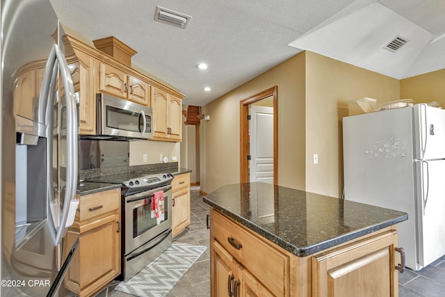 kitchen featuring a center island, light brown cabinets, dark stone counters, a textured ceiling, and stainless steel appliances