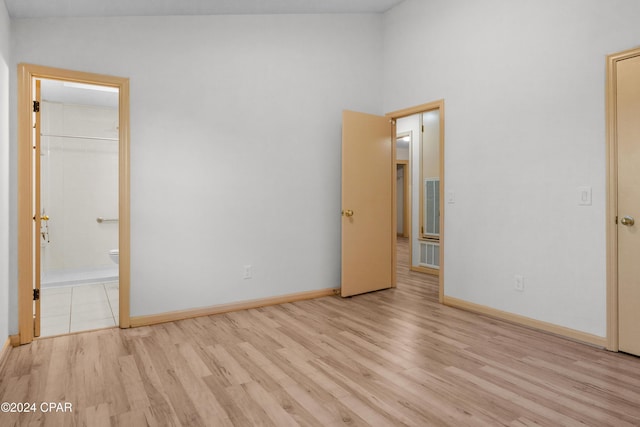 unfurnished bedroom with connected bathroom, a walk in closet, a closet, and light hardwood / wood-style flooring