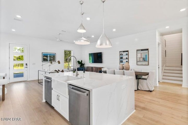 kitchen featuring dishwasher, a center island with sink, light hardwood / wood-style flooring, decorative light fixtures, and white cabinetry