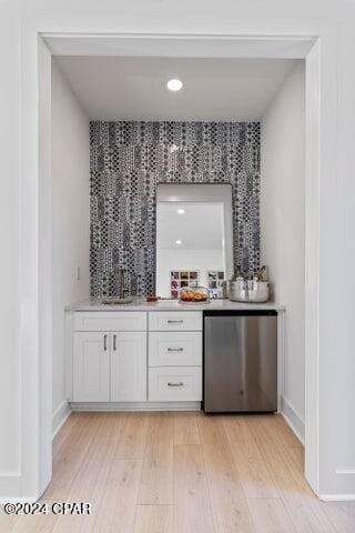 bar featuring light hardwood / wood-style flooring, white cabinets, fridge, and sink