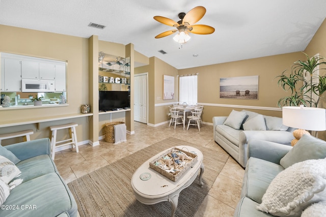 living room featuring ceiling fan, light tile patterned flooring, lofted ceiling, and a textured ceiling