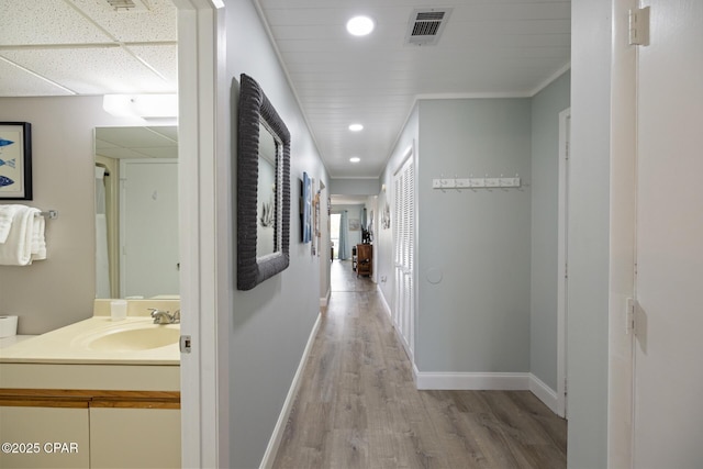 hall with sink, a paneled ceiling, and light wood-type flooring