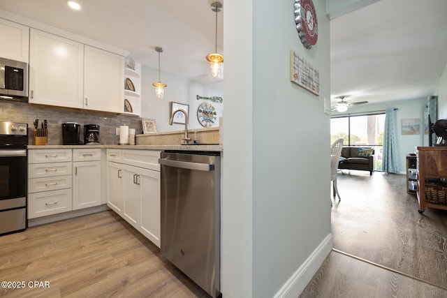 kitchen with appliances with stainless steel finishes, backsplash, white cabinets, decorative light fixtures, and light wood-type flooring