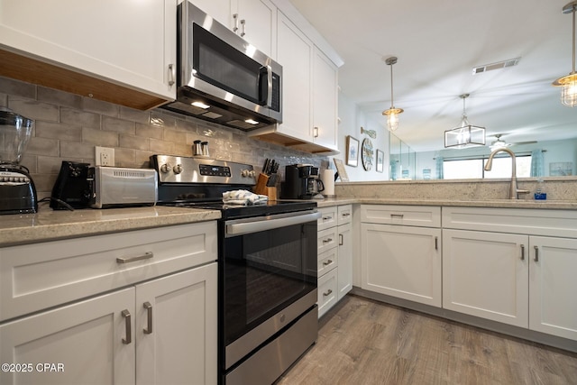 kitchen with sink, appliances with stainless steel finishes, white cabinetry, hanging light fixtures, and decorative backsplash