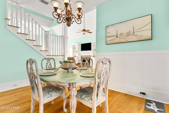 dining area with ceiling fan with notable chandelier, wood-type flooring, and lofted ceiling