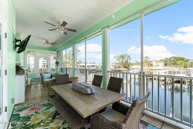 sunroom with ceiling fan and a water view