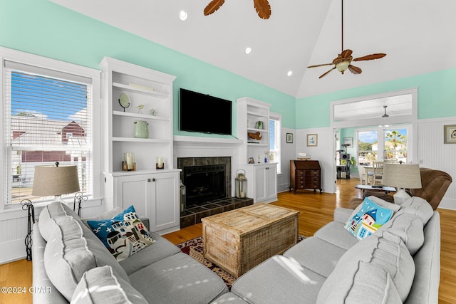 living room with a tile fireplace, hardwood / wood-style flooring, high vaulted ceiling, and ceiling fan