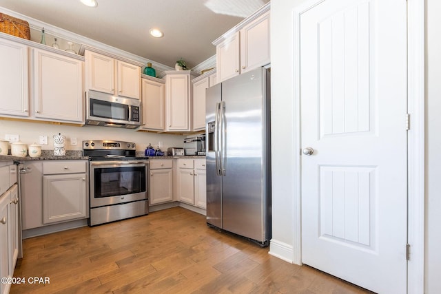 kitchen featuring light wood-style flooring, recessed lighting, stainless steel appliances, ornamental molding, and dark stone countertops