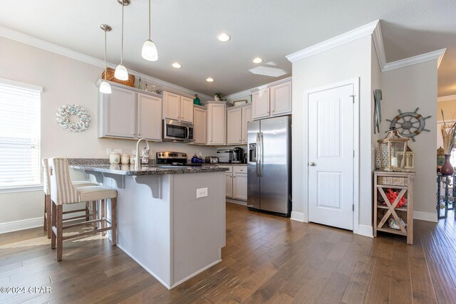 kitchen featuring dark wood-style floors, a breakfast bar, stainless steel appliances, ornamental molding, and a peninsula