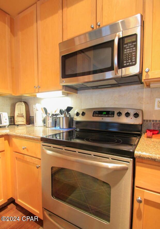 kitchen with decorative backsplash, light stone counters, stainless steel appliances, and wood-type flooring