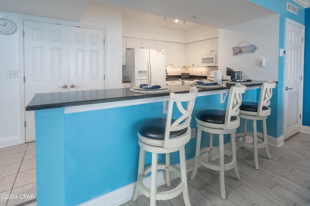 kitchen featuring white cabinetry, a kitchen breakfast bar, white appliances, and light hardwood / wood-style flooring