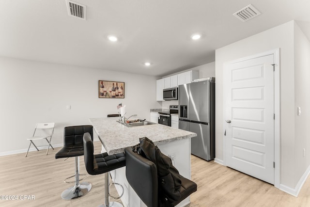 kitchen featuring white cabinets, sink, light hardwood / wood-style flooring, an island with sink, and stainless steel appliances