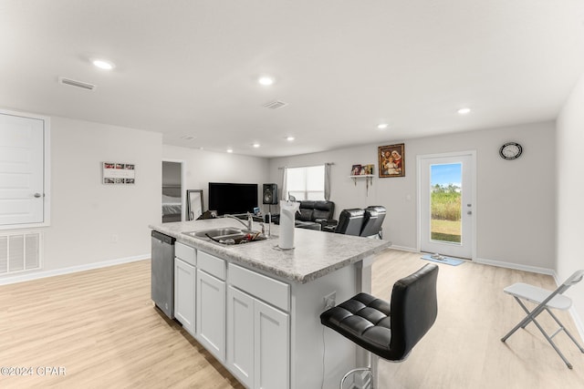 kitchen with white cabinets, sink, stainless steel dishwasher, light wood-type flooring, and an island with sink