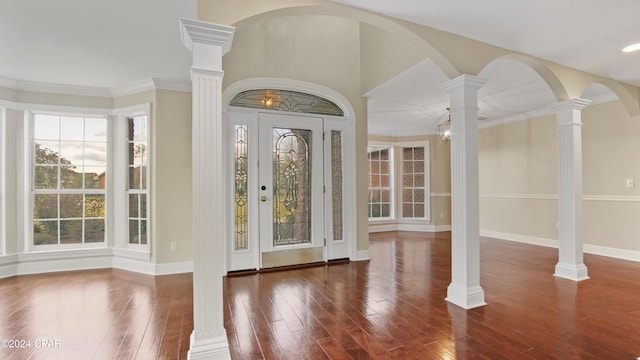 entrance foyer featuring dark hardwood / wood-style floors, ornamental molding, ornate columns, and an inviting chandelier